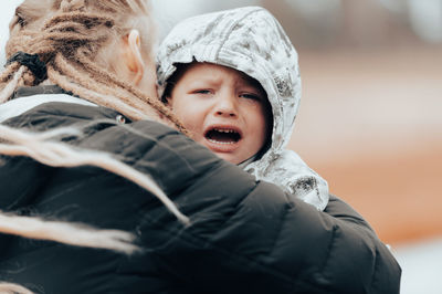 Mother holding crying baby, sad little boy being hugged by his mother