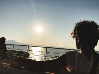 Rear view of man looking at sea against clear sky during sunset