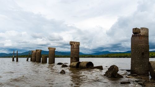 Wooden posts in sea against sky