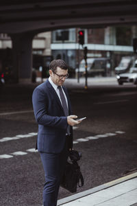 Businessman with bag using smart phone while standing in city