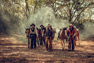 Men with horses walking on land in forest