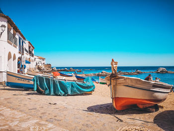 Boats moored on beach against clear blue sky