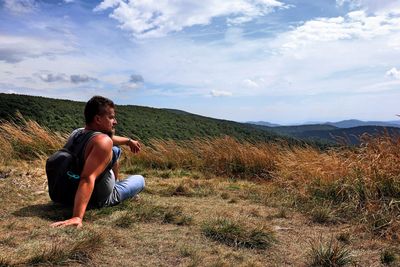 Man sitting on grass against sky