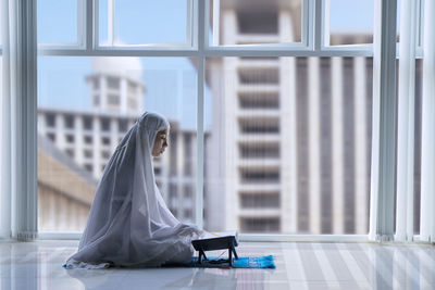 Side view of woman reading koran on floor