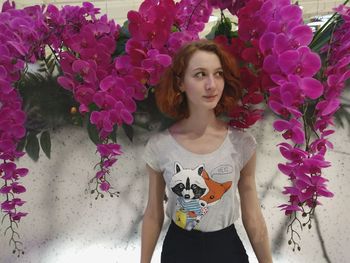 Portrait of beautiful young woman standing against flowers