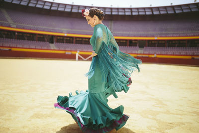 Young woman wearing blue dress flamenco dancing in bullring