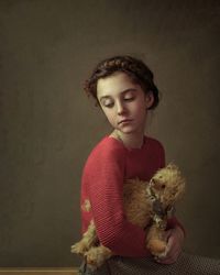 A girl with dark hair pigtail around her head red sweater standing holding her teddy bear toy hands