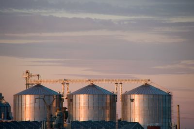 Factory by sea against sky during sunset