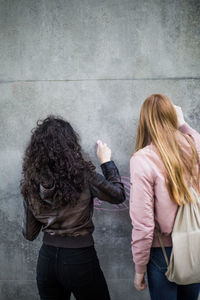 Rear view of female friends drawing on gray wall