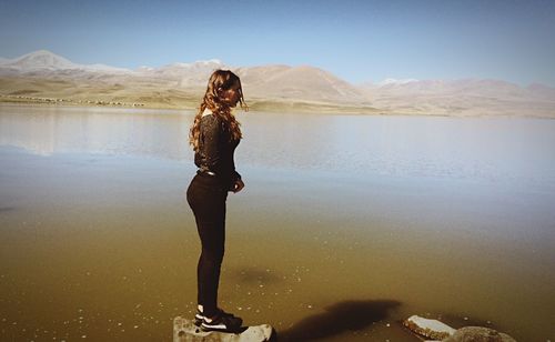 Side view of young woman standing on rock in lake