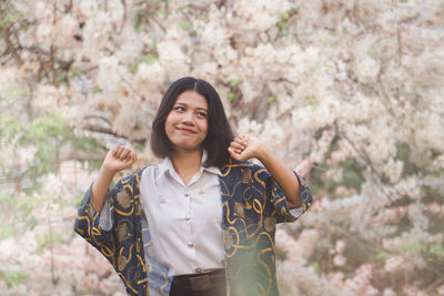 Portrait of smiling young woman standing against trees