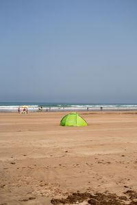 Green tent on the beach with few people walking around