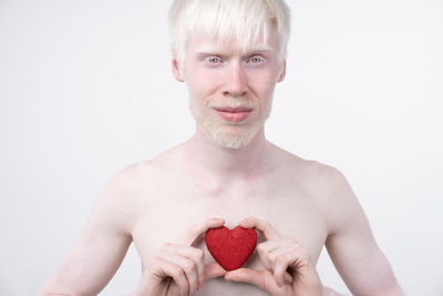 Portrait of shirtless man holding heart shape against white background