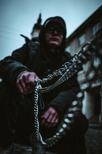 Full length of young man holding chain crouching on street