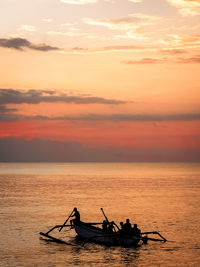 Silhouette people on boat in sea against sky during sunset