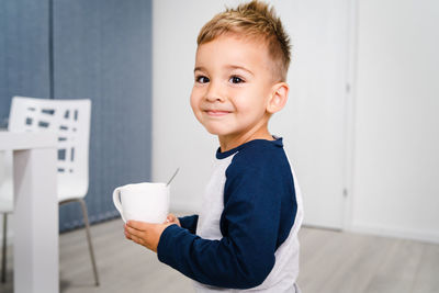 Portrait of boy having drink in cup while standing at home