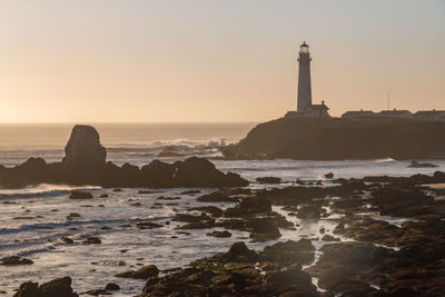 Lighthouse by sea against sky during sunset