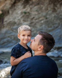 Like father like son. middle aged father embracing cute little son on the bank of river