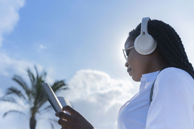 Young woman using mobile phone against sky