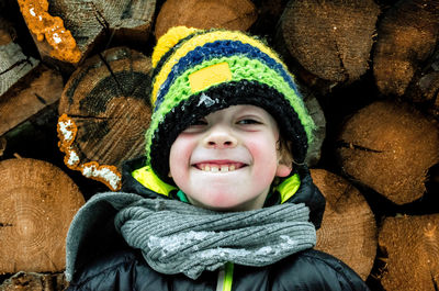 Close-up of smiling boy standing against logs