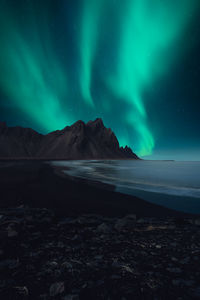 Scenic view of sea by mountains against sky at night