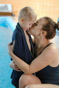 Toddler child hugging mother after swimming in indoor swimming pool wrapped in towel.