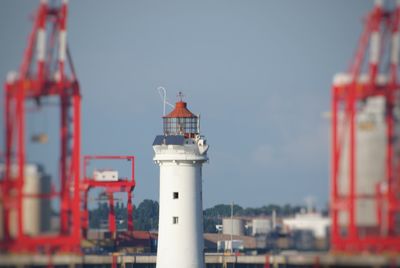 Lighthouse by buildings against sky