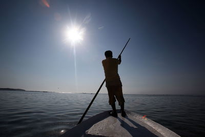 Man rowing boat in river against sky on sunny day