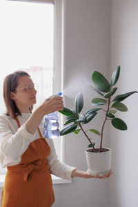 Side view of young woman holding potted plant at home