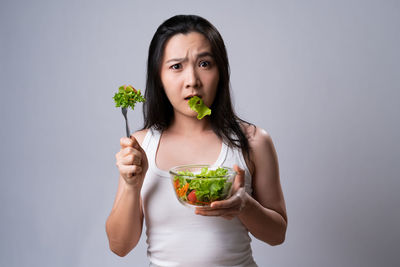 Portrait of woman holding ice cream against gray background