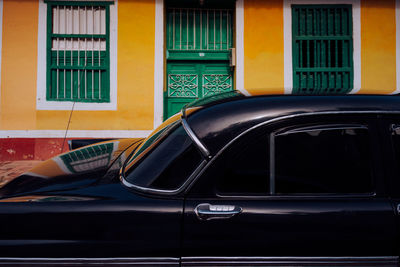 Small street with black vintage car in roadside between historical colorful buildings with bars on windows in cuba