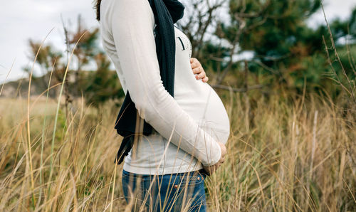 Midsection of pregnant woman standing on field