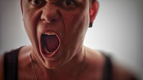 Close-up of angry young man with mouth open against white background