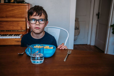 Young boy frowning at the table while eating a meal