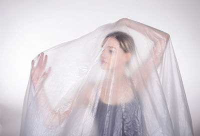 Close-up of woman covered in plastic against white background