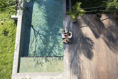 Family sitting at the swimming pool, mother reading book for children