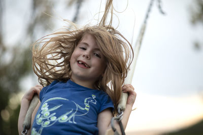 Low angle portrait of smiling girl sitting on swing