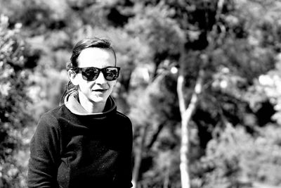 Portrait of woman wearing sunglasses standing against trees