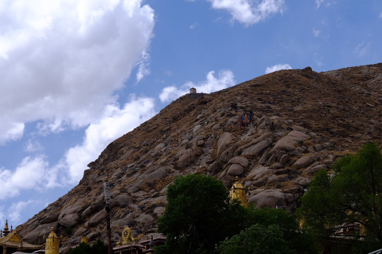 sky, rock formation, low angle view, cloud - sky, rock - object, mountain, cloud, tranquility, nature, tree, cliff, rocky mountains, tranquil scene, blue, beauty in nature, scenics, geology, day, sunlight, non-urban scene