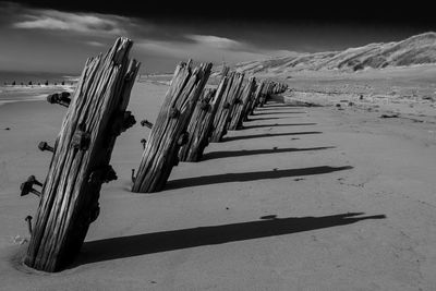 Abandoned wooden posts at beach by mountains against sky