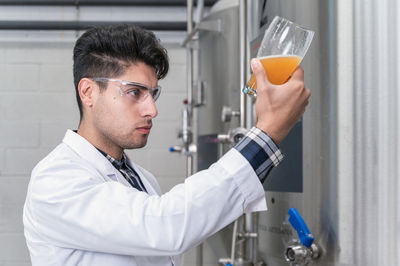 Young man inspecting beer in factory