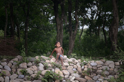 Full length of shirtless man standing on rocks by trees