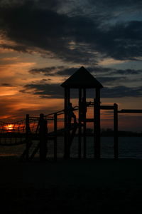 People on jungle gym at beach against sky during sunset