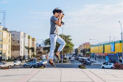 Side view of man photographing while levitating in city