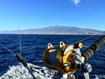 Close-up of fishing rod with sea in background against blue sky