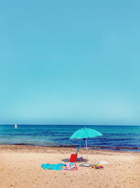 Lounge chairs and parasols on beach against clear blue sky