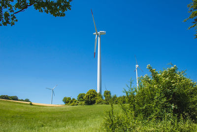 Low angle view of wind turbines on field against clear sky