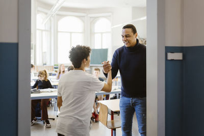 Smiling male teacher doing handshake with student in classroom