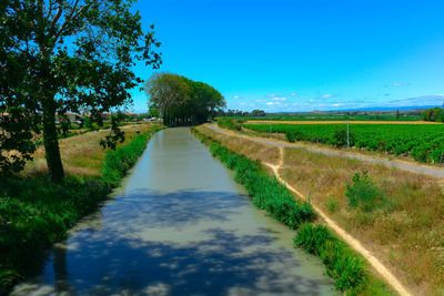 Road amidst field against clear blue sky