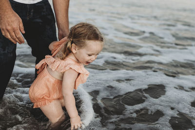 Toddler girl splashing in ocean with father at sunset